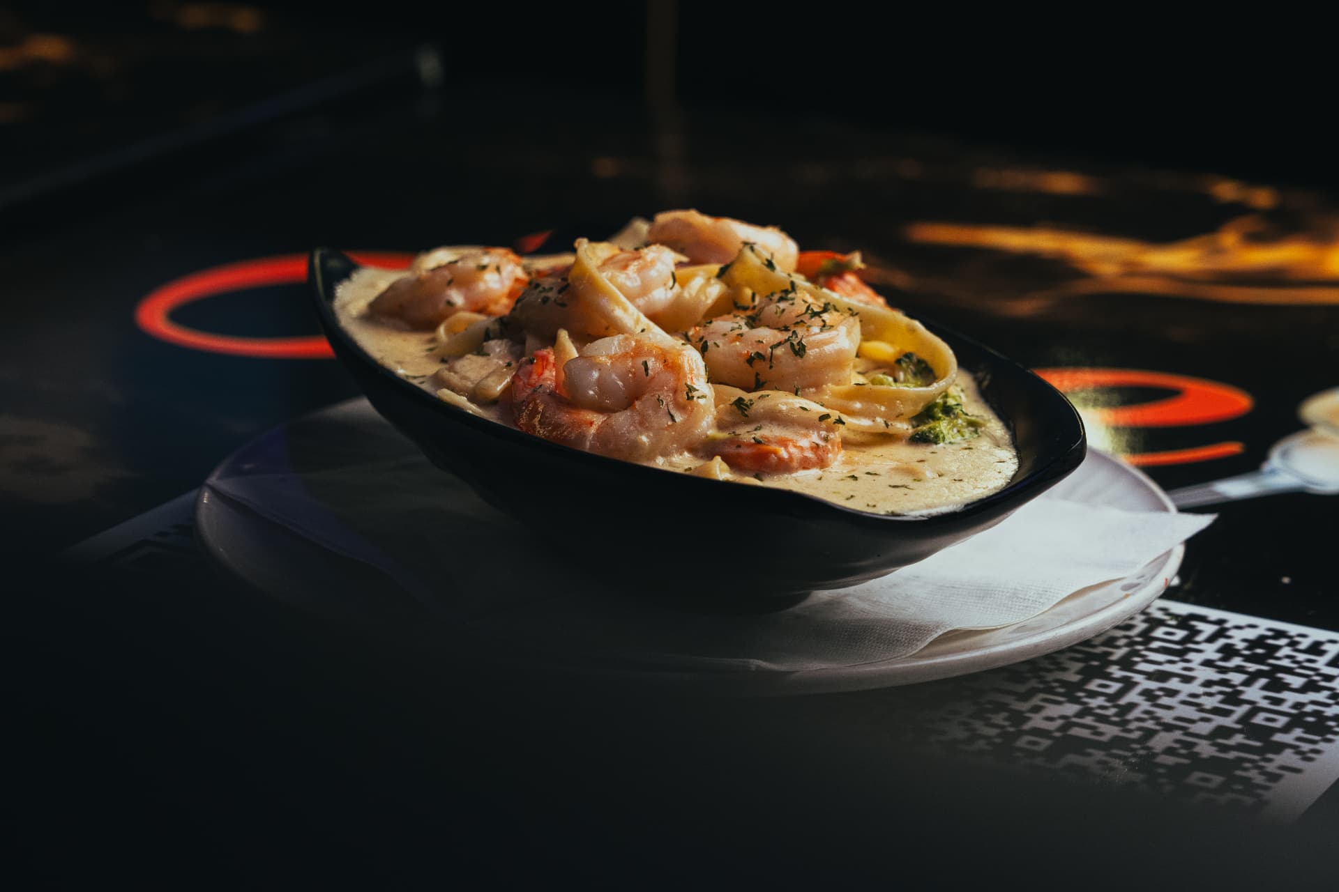 Creamy shrimp pasta in a black bowl under neon light at Joey's Restaurant